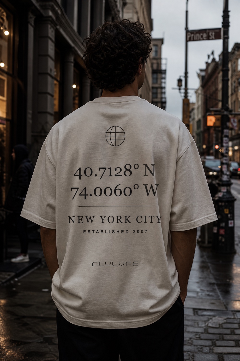 FLYLYFE Coordinates tee — NYC latitude and longitude back print, worn on a model in NYC
